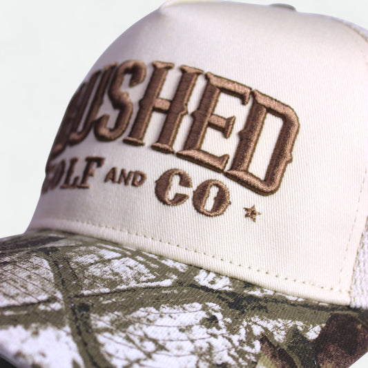 Close-up of embroidered Flushed Golf & Co logo on trucker hat with camo brim
