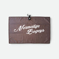 A brown textured waffle golf towel with white script text reading 'Normalize Bogeys' and a small black hanging loop at the top, shown on a light grey background.