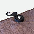 A close-up of a black circular carabiner clip and magnet with a white 'FG' logo, attached to a brown waffle golf towel.