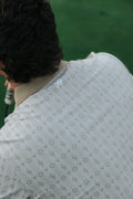 Close-up back view of a person wearing a tan cactus country patterned polo shirt on a green turf background.